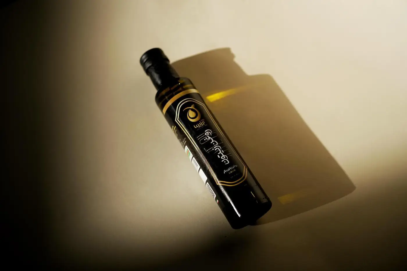 Arzima olive oil bottle casting a long shadow on a dark backdrop